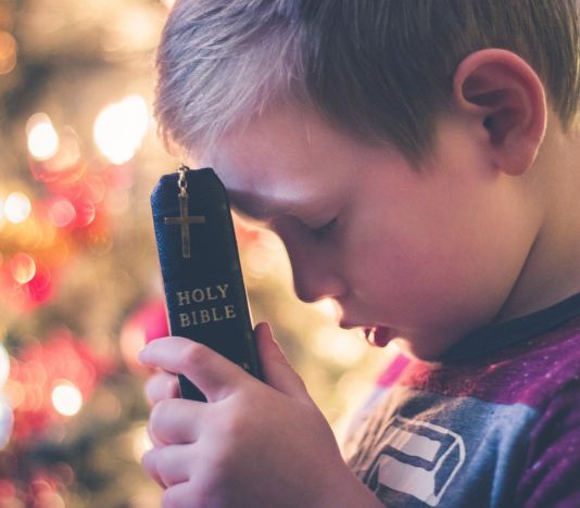 criança com biblia encostando na testa